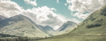 Bild eines grünen Tals mit blauem, teils bewölktem Himmel