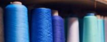 Background with a lot of blue coils with threads. Bobbins are stacked in a rows, one on the other. Selective focus.